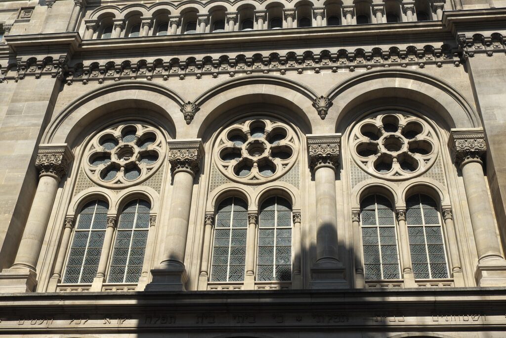 The stone façade of the Grande Synagogue de la Victoire in Paris, with rose windows and a Hebrew inscription
